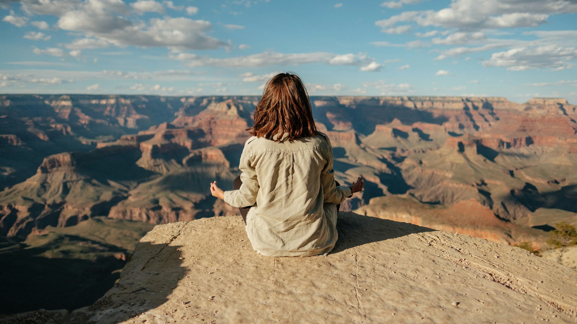 Representation of body-mind-soul connection. A woman sitting on mountain top in sunshine with a beautiful view.