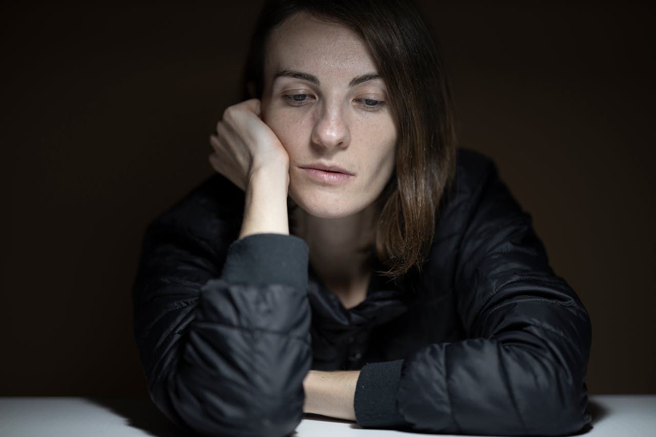 Woman experiencing depression with hand on her face looking downwards.